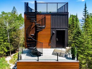 Uma cabana moderna com escada em espiral, um deck e uma porta.