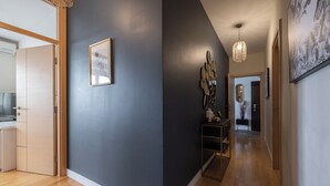 Un couloir avec un mur sombre, un plancher en bois, un luminaire suspendu et un tableau encadré.