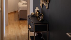 Une chambre d’hôtel moderne avec un mur de couleur sombre, un luminaire suspendu, un mur miroir et une table de chevet agrémentée d’une horloge et d’objets décoratifs.