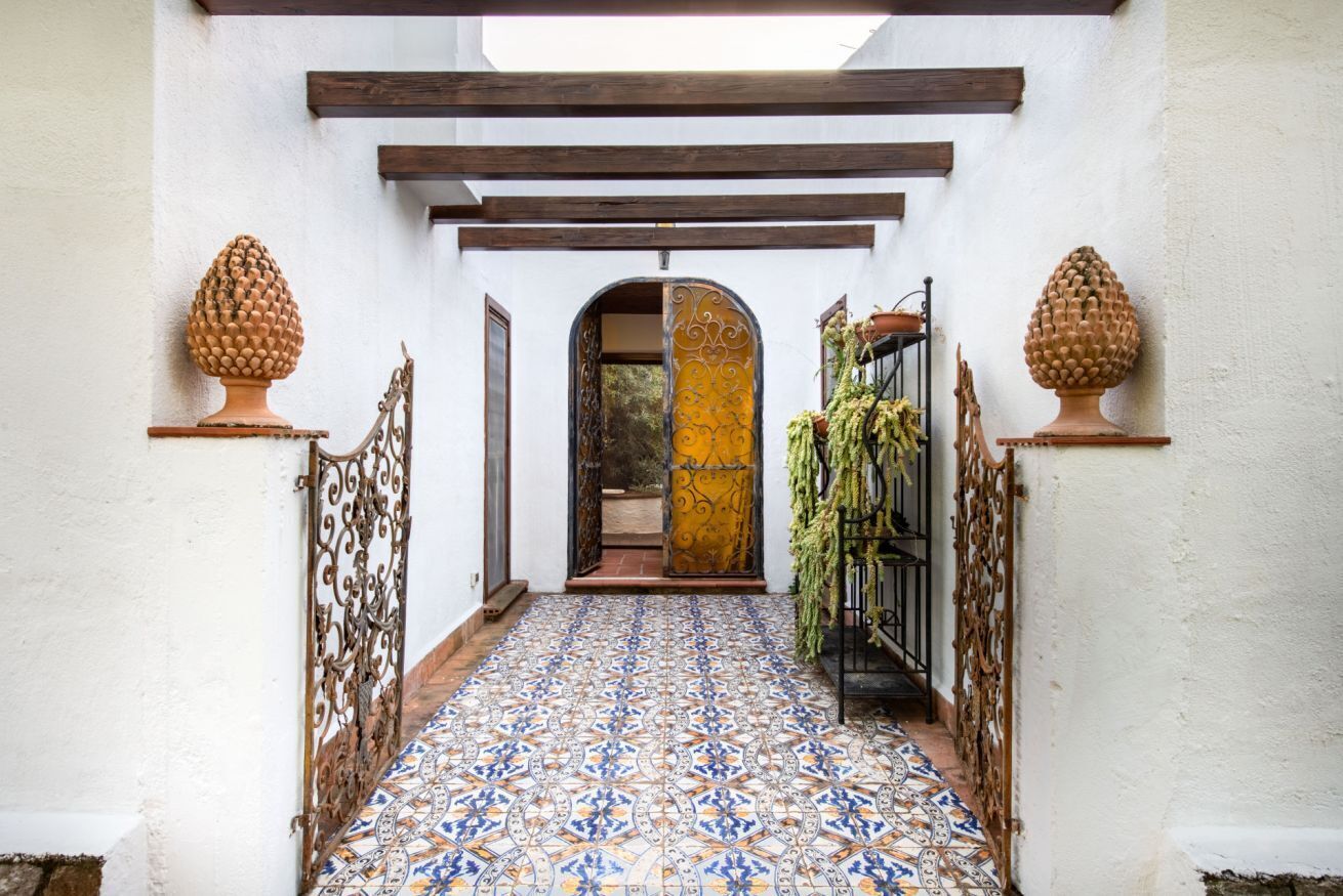 A hallway with patterned tile flooring, a wooden ceiling, and decorative urns on pedestals.