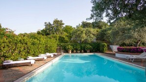 Une piscine rectangulaire à l’eau d’un bleu limpide, entourée d’une terrasse carrelée. On y trouve des chaises longues et une petite structure blanche, qui pourrait être un vestiaire ou un local de rangement, à proximité de la piscine.