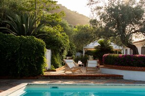 Zona de piscina con vista despejada, rodeada de vegetación exuberante y un edificio blanco con patio.