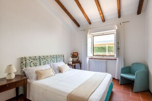 Une chambre à coucher comprenant un lit, une table de chevet, une chaise, une fenêtre avec des rideaux et une vue sur la verdure à l’extérieur.