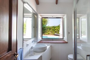 Un baño moderno con un ventanal grande, un lavabo redondo y un inodoro.