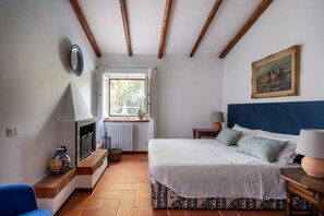 Un dormitorio con cama, ventana, chimenea y un cuadro en la pared.