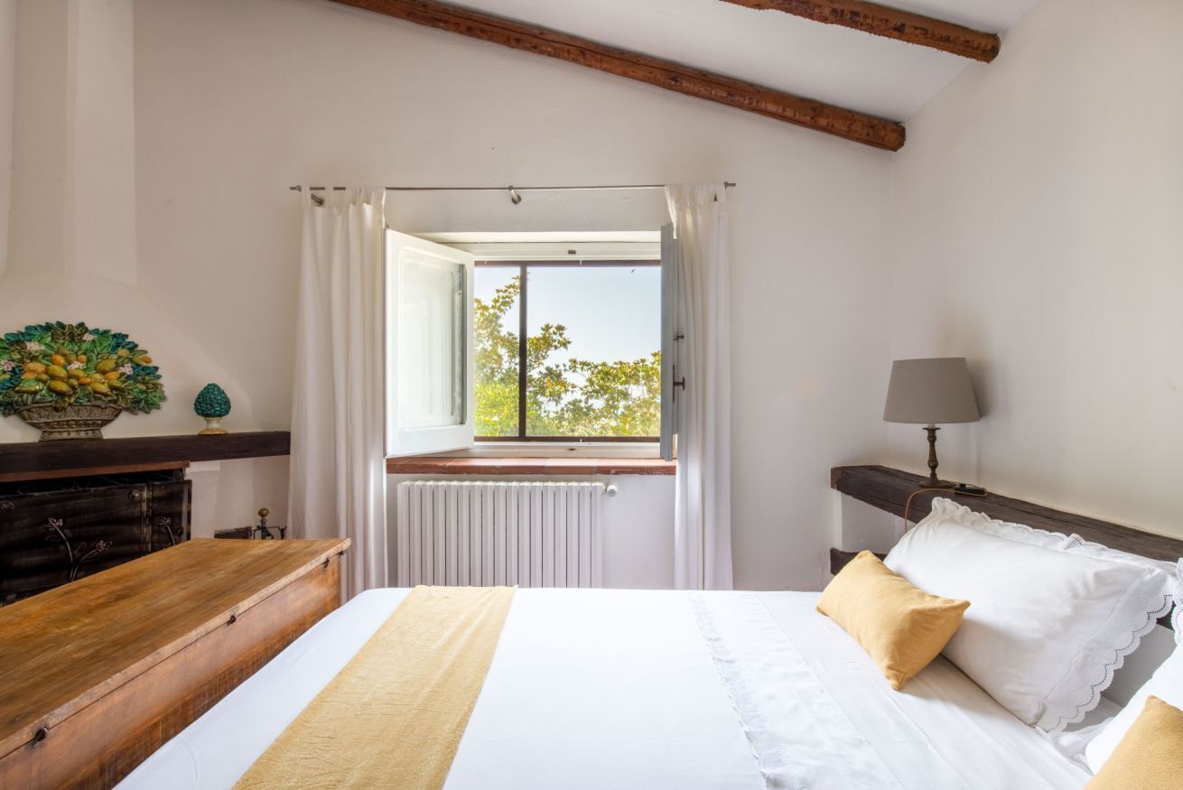 Un dormitorio con una cama grande, un aparador de madera, una ventana con cortinas y vista a árboles fuera.
