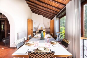 Comedor con una mesa larga dispuesta para una comida, vigas de madera en el techo y vista a zonas verdes al exterior.