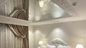 A bedroom with a large bed, two bedside tables, a pink ottoman, and a chandelier. - Rox luxury Hotel (Taif)