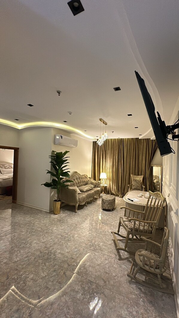 A spacious living room with a marble floor, a sofa set, a dining table with chairs, and a chandelier. - Rox luxury Hotel (Taif)