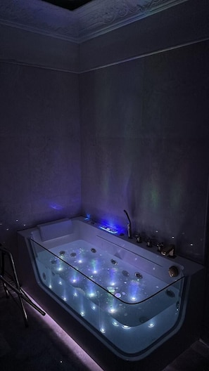 A modern bathroom with a glass-enclosed bathtub, blue ambient lighting, and a sleek design.