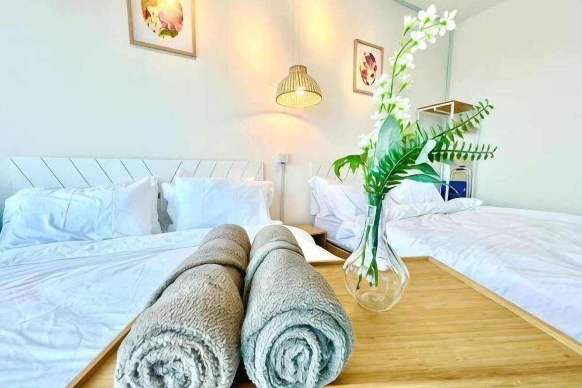 A hotel room with two beds, a wooden tray with towels, a vase with flowers, and wall-mounted lamps.