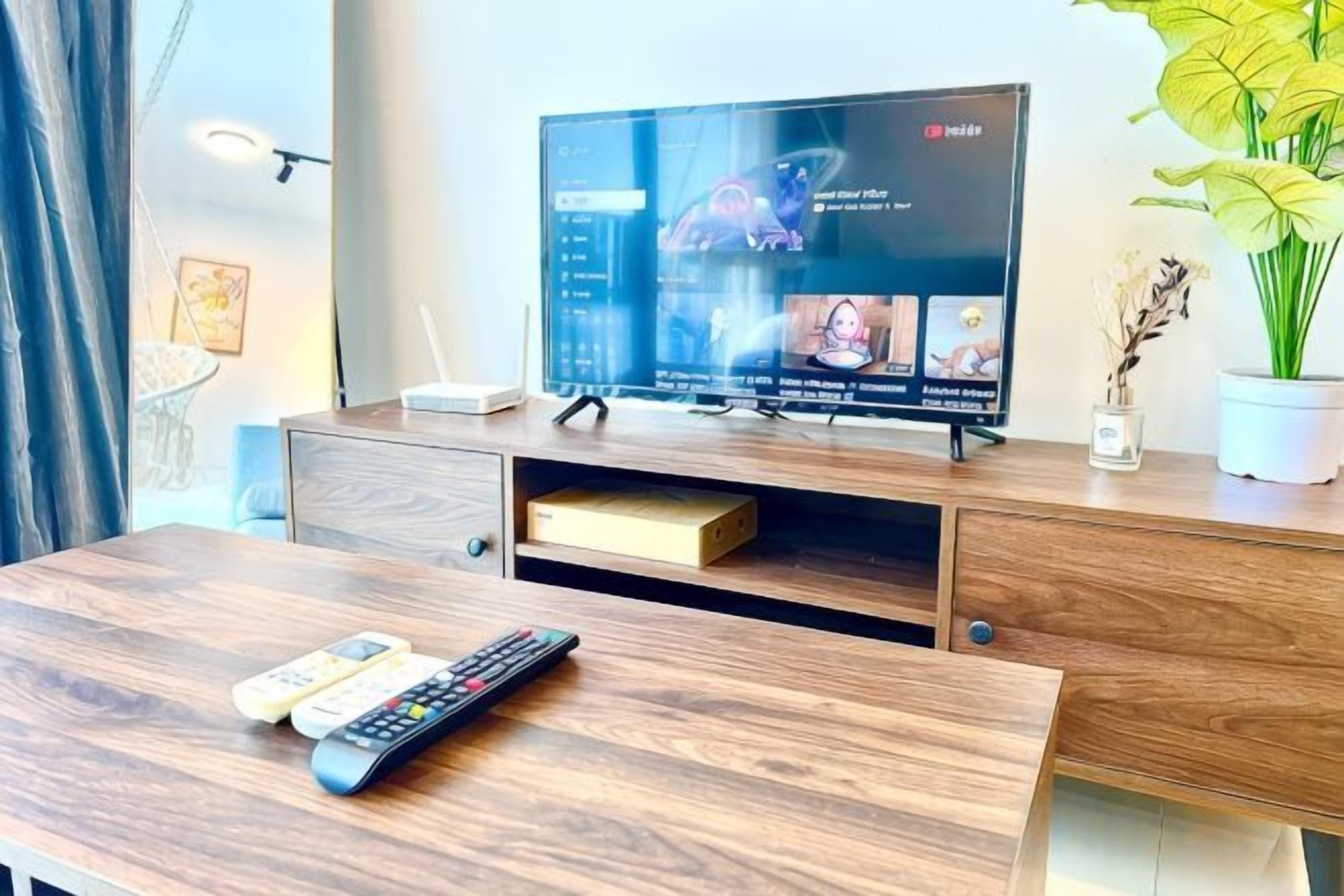 A modern living room with a flat-screen TV, wooden furniture, and a potted plant.