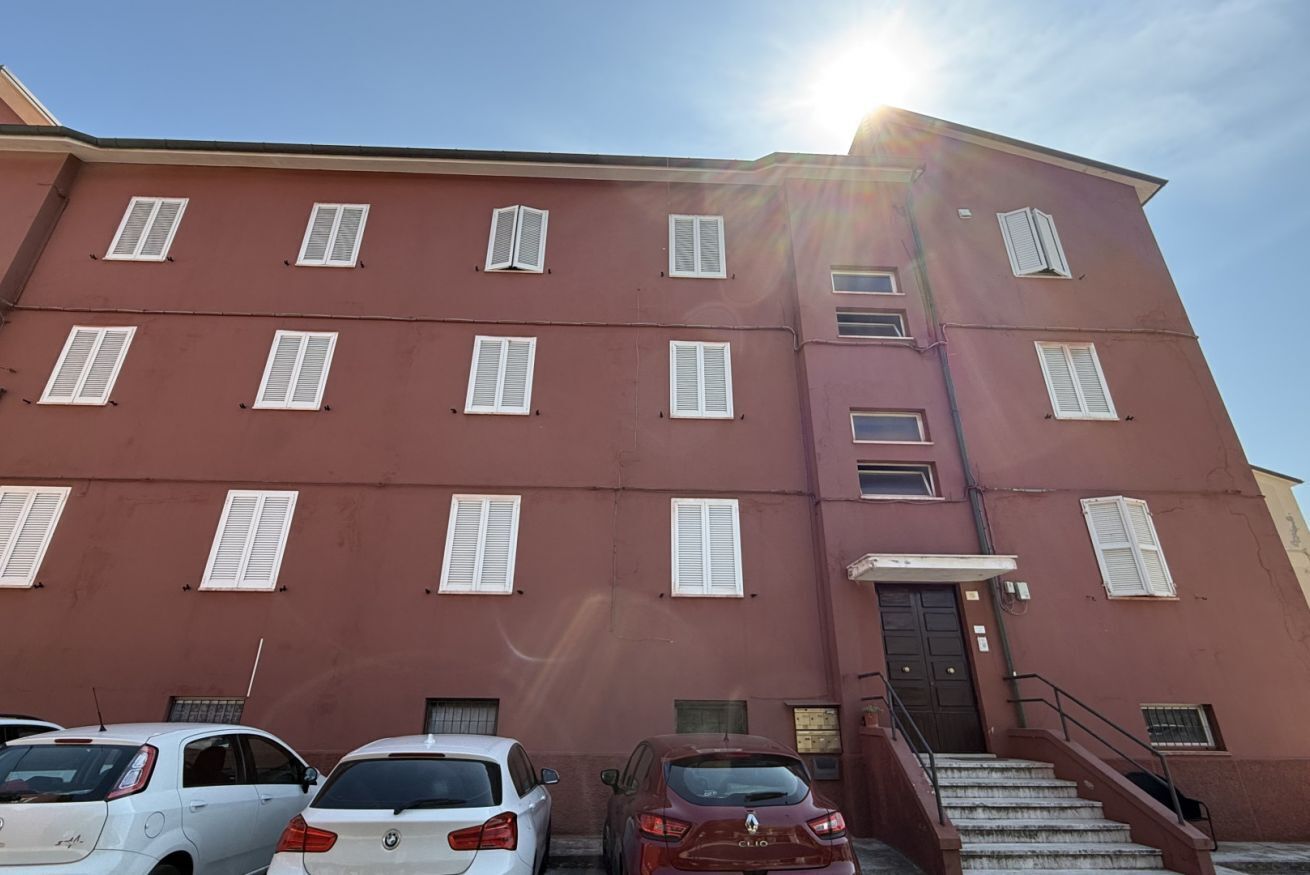 Ein mehrstöckiges Gebäude mit roter Fassade, weißen Fensterläden und einer Treppe, die zum Eingang führt.