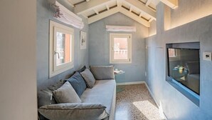 A cozy room with a gray sofa, two windows, a TV, and a ceiling with exposed beams. - House with canal view (Venezia)