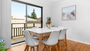 A dining area with a white table and chairs, a vase with flowers, and a framed picture on the wall. - Verzelha by the Sea - Spacious 3BR Family Stay in Culburra (Culburra Beach)