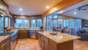 Una cocina amplia con una isla grande, armarios de madera y vistas al exterior a través de amplios ventanales.
