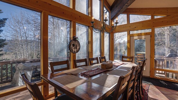 Un comedor de madera con ventanas amplias, una araña y vistas al exterior.