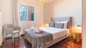 Ein Schlafzimmer mit Bett, Stuhl, Fenster und einer Pendelleuchte.