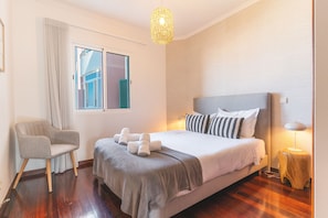 Ein Schlafzimmer mit Bett, Stuhl, Fenster und einer Pendelleuchte.