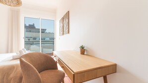 Ein modernes Zimmer mit einem Bett, einem Schreibtisch, einem Sessel, einer Topfpflanze und einem großen Fenster mit Blick.