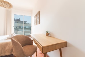 Ein modernes Zimmer mit einem Bett, einem Schreibtisch, einem Sessel, einer Topfpflanze und einem großen Fenster mit Blick.