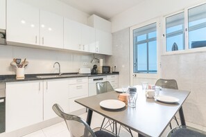 Una cocina moderna con armarios blancos, una mesa de comedor con platos, vasos y una cafetera.