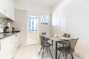 A modern kitchen with white cabinets, a dining table with chairs, and a view through a glass door. - Lido Vista Apartment by Atlantic Holiday (Funchal)