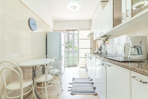 A modern kitchen with white cabinets, a coffee machine, and a dining area with chairs and a table. - Forum Delights Apartment by Atlantic Holiday (Funchal)
