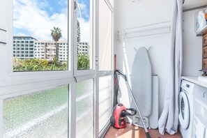 A laundry area with a washing machine, ironing board, and a vacuum cleaner. - Forum Delights Apartment by Atlantic Holiday (Funchal)