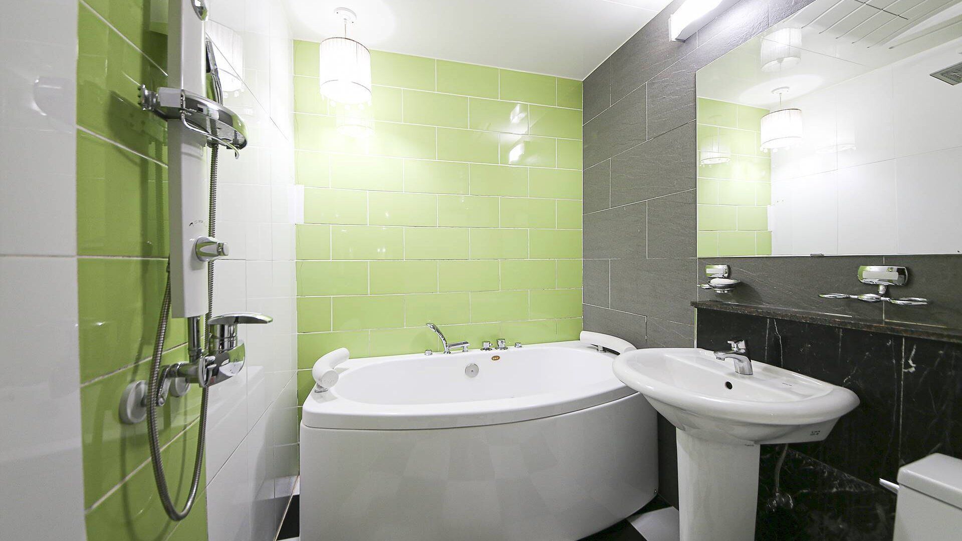 A bathroom with a shower, two sinks, and green and gray tiled walls.