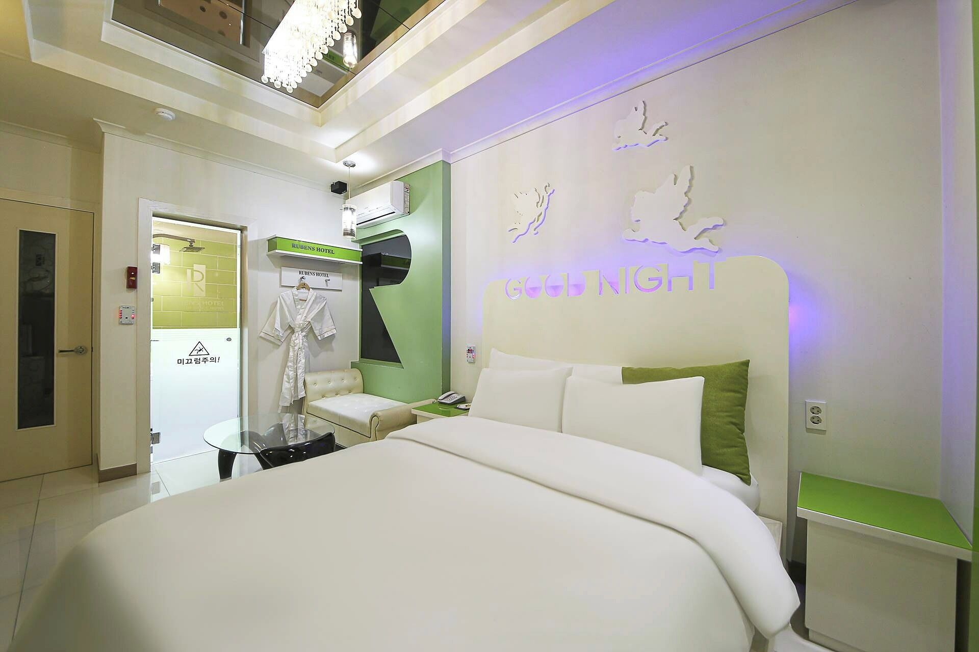 A hotel room with a large bed, a nightstand, a robe, and a wall with a 'GOOD NIGHT' sign.