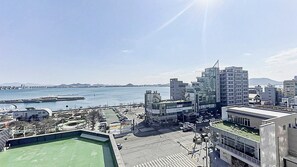 A cityscape with a view of the sea, featuring modern buildings, a parking lot, and a green-roofed structure. - From H Rubens Hotel Mokpo Pyeonghwa Square (Mokpo)
