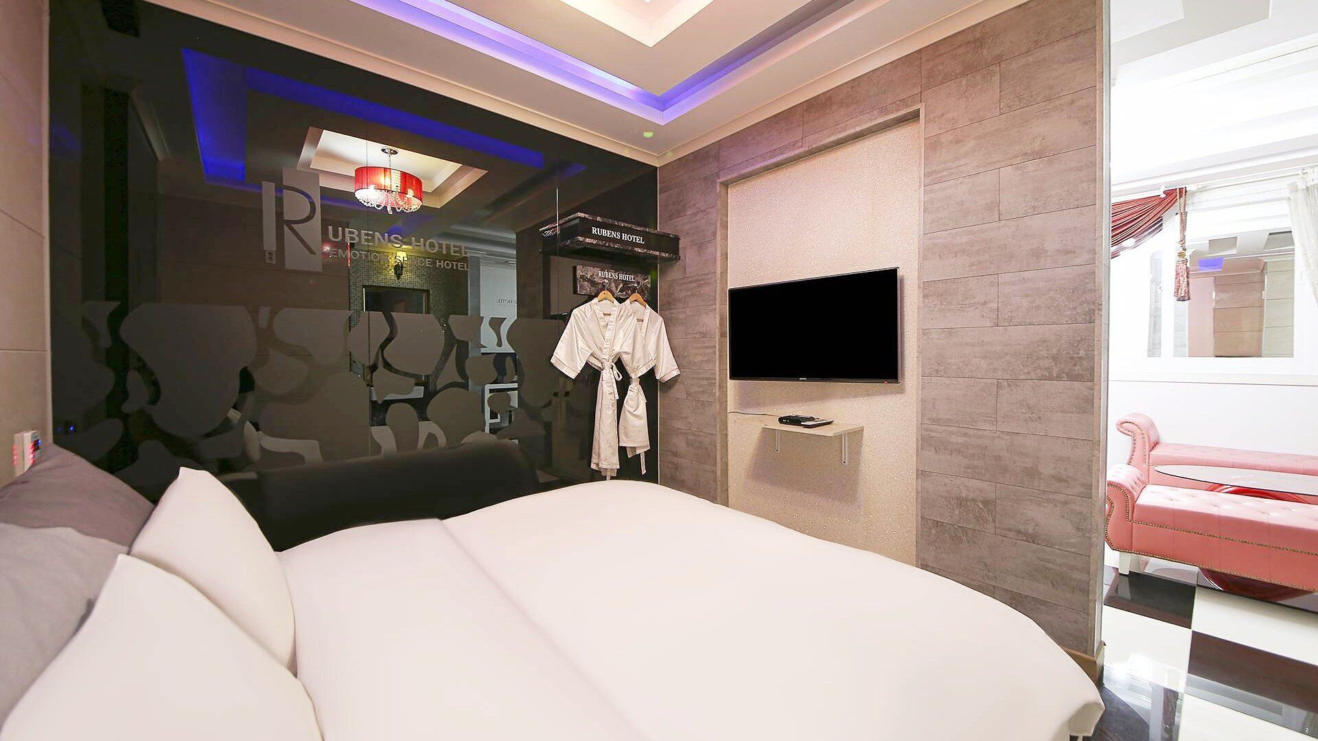 A modern hotel room with a large bed, a flat-screen TV mounted on the wall, and a minibar.