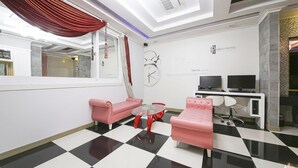 A hotel room with a checkered floor, two pink sofas, a glass coffee table, a desk with two monitors, and a red curtain. - From H Rubens Hotel Mokpo Pyeonghwa Square (Mokpo)