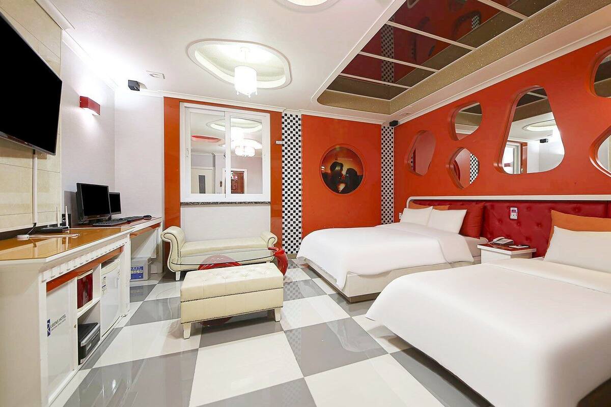 Ein Hotelzimmer mit zwei Betten, einem Fernseher, einem Schreibtisch und einem Schachbrettmuster-Boden.