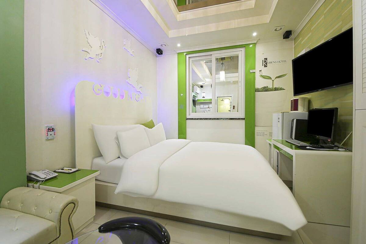 Ein modernes Hotelzimmer mit einem Bett, einem Schreibtisch mit Computer, einem Fernseher und einer Wand in Grüntönen.