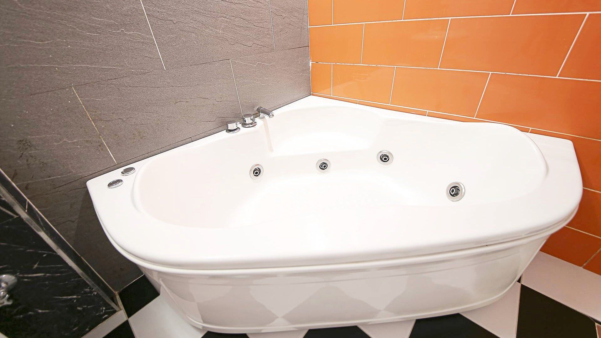 A white freestanding bathtub in a bathroom with a black and white checkered floor, grey stone walls, and orange tiles.