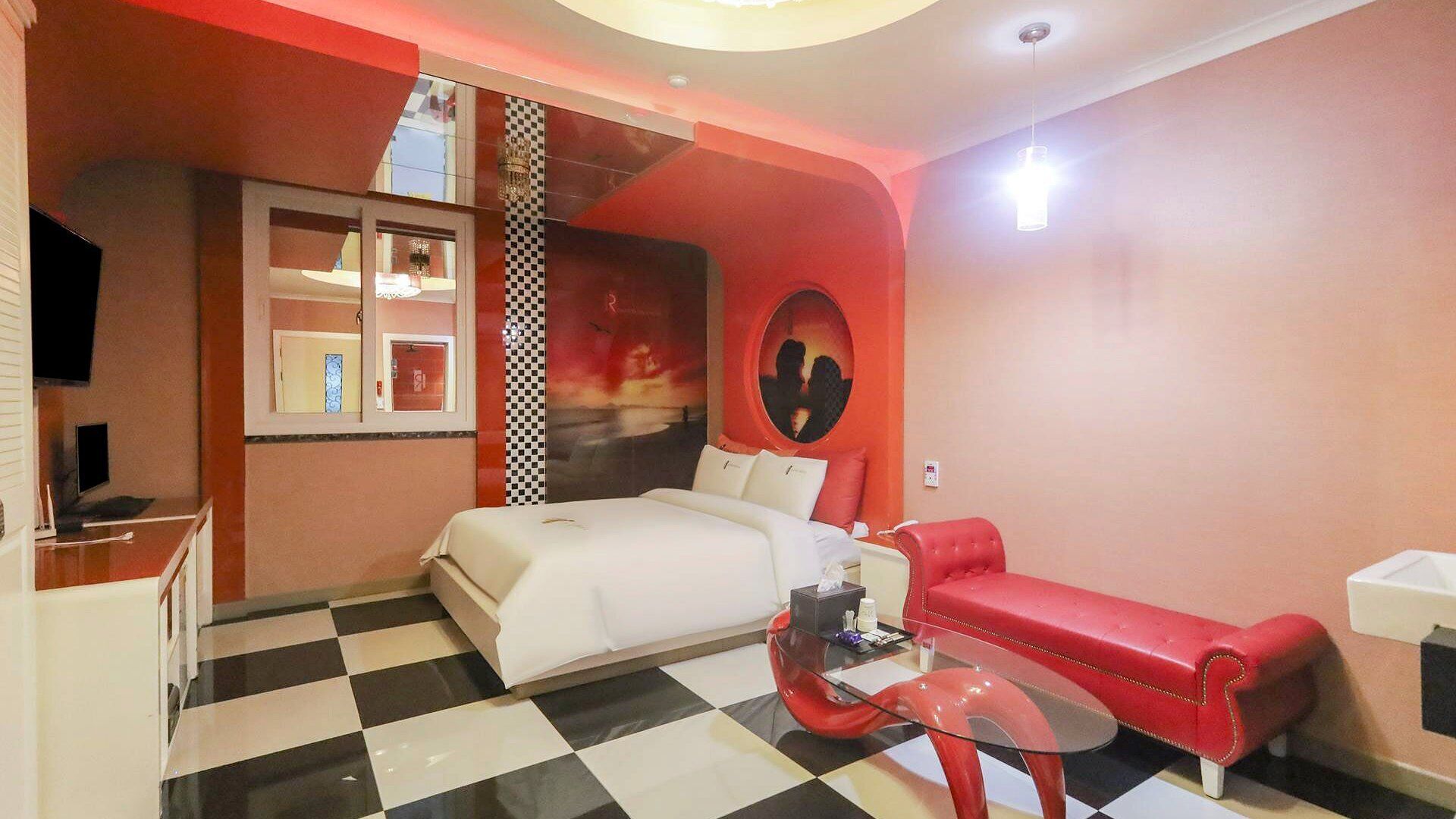 Habitació d'hotel amb terra de pissos, un llit, un sofà vermell, una taula de café de vidre i un televisor sobre un moble.