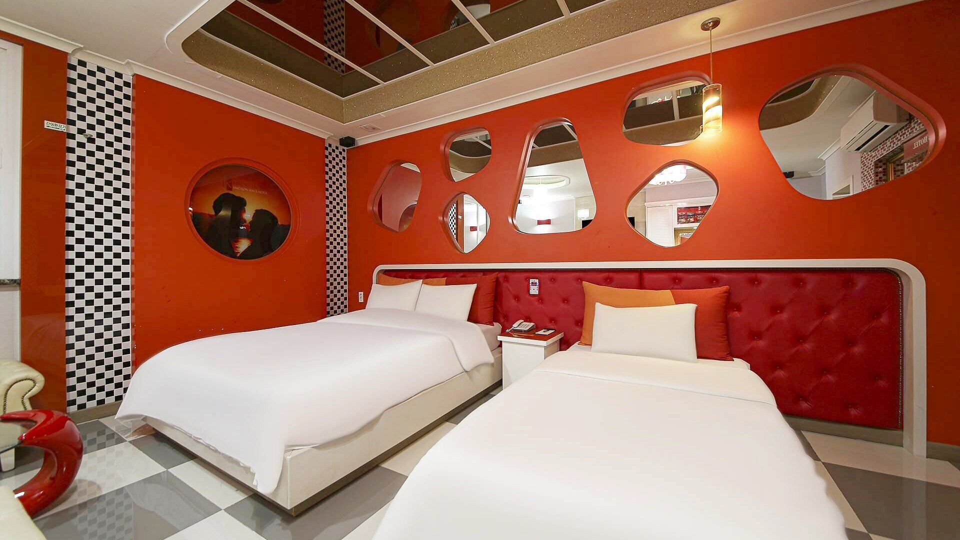 Habitación de hotel con dos camas, un cabecero tapizado en rojo y varios espejos en las paredes.