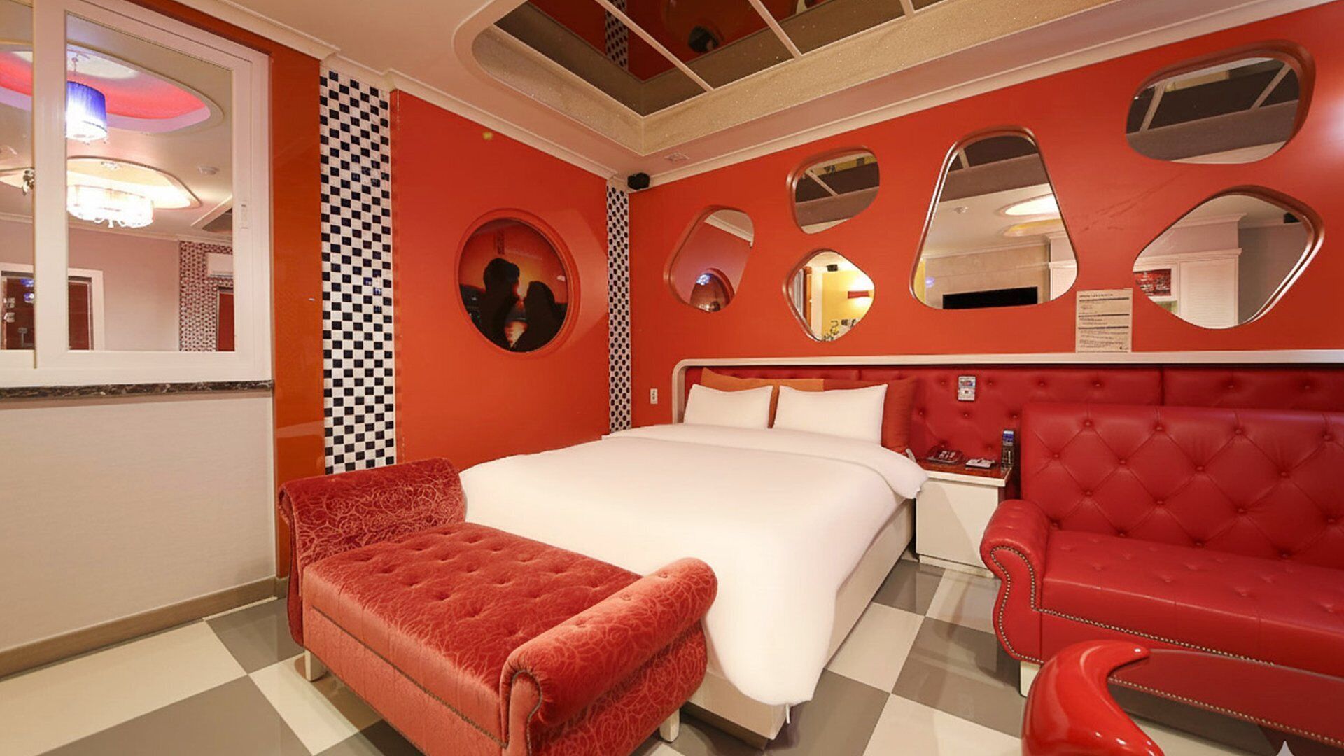 A hotel room with a large bed, a red armchair, and a red sofa.
