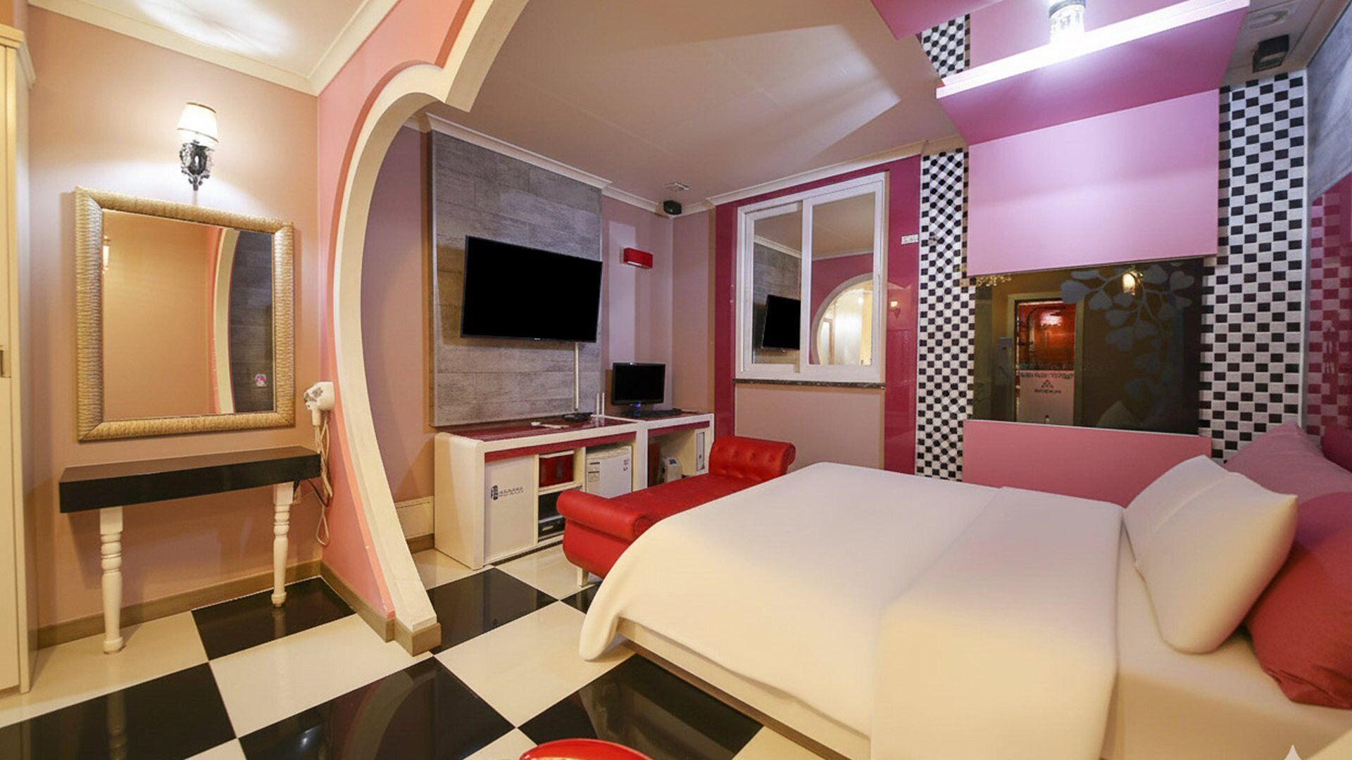 Una habitación de hotel moderna con una cama grande, un escritorio con una computadora, un televisor y un espejo.