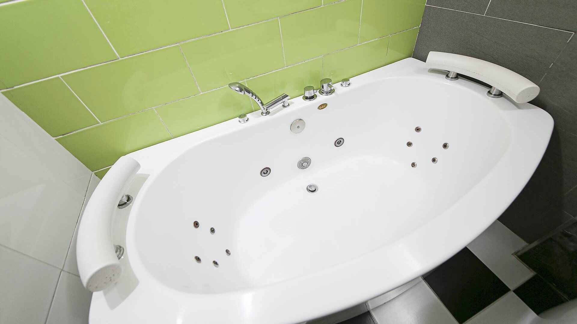 A white bathtub with multiple jets, a handheld showerhead, and a control panel with several knobs.