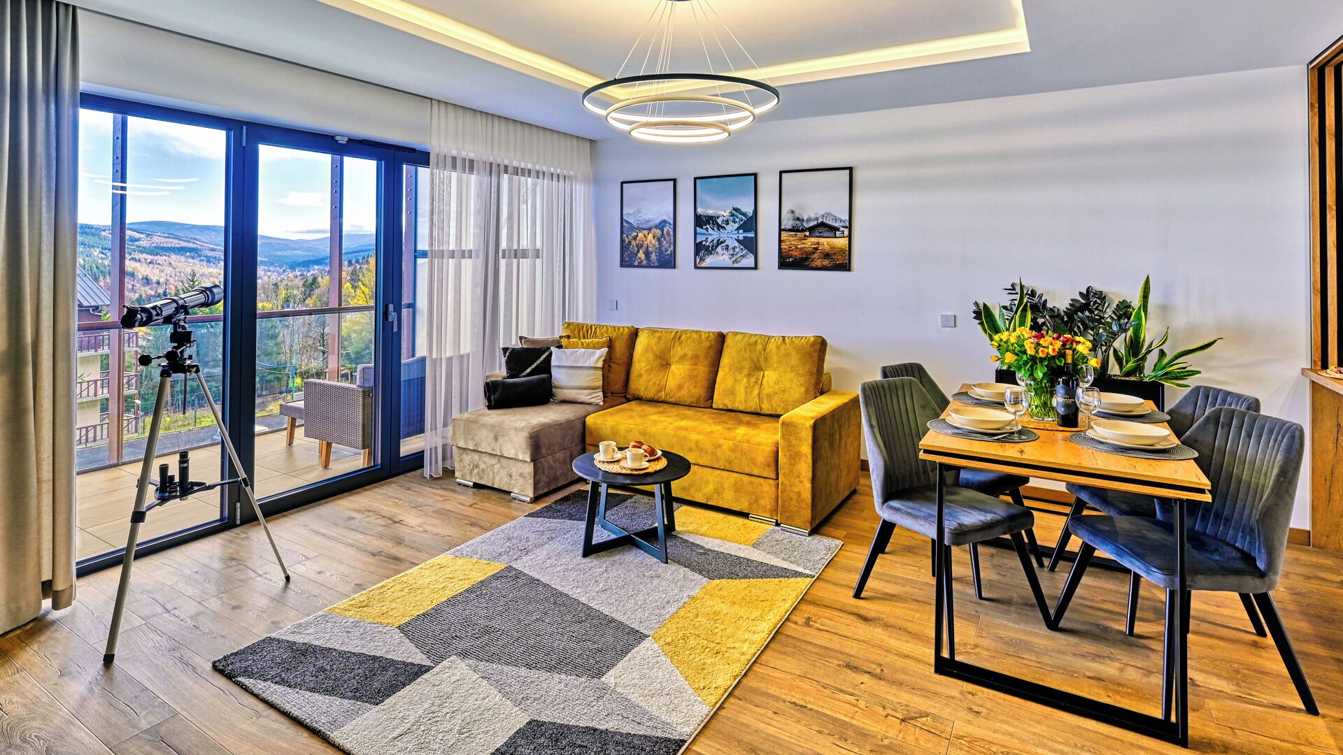 A modern living room with a sofa, dining table, and chairs, a telescope, and a large window with a view.