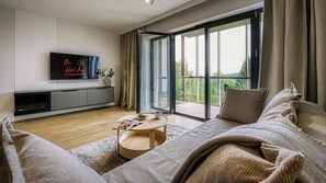 A modern living room with a flat-screen TV, a sofa, a coffee table, and a sliding glass door leading to a balcony. - Apartamenty Żródło Izery - by OnHoliday (Świeradów-Zdrój)