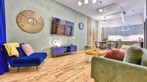 A modern living room with a sofa, a television, a clock, and a dining area with a table and chairs. - Apartamenty Żródło Izery - by OnHoliday (Świeradów-Zdrój)