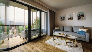 A modern living room with a large sliding glass door leading to a balcony, a grey sofa, a round coffee table, and framed artwork on the wall. - Apartamenty Żródło Izery - by OnHoliday (Świeradów-Zdrój)