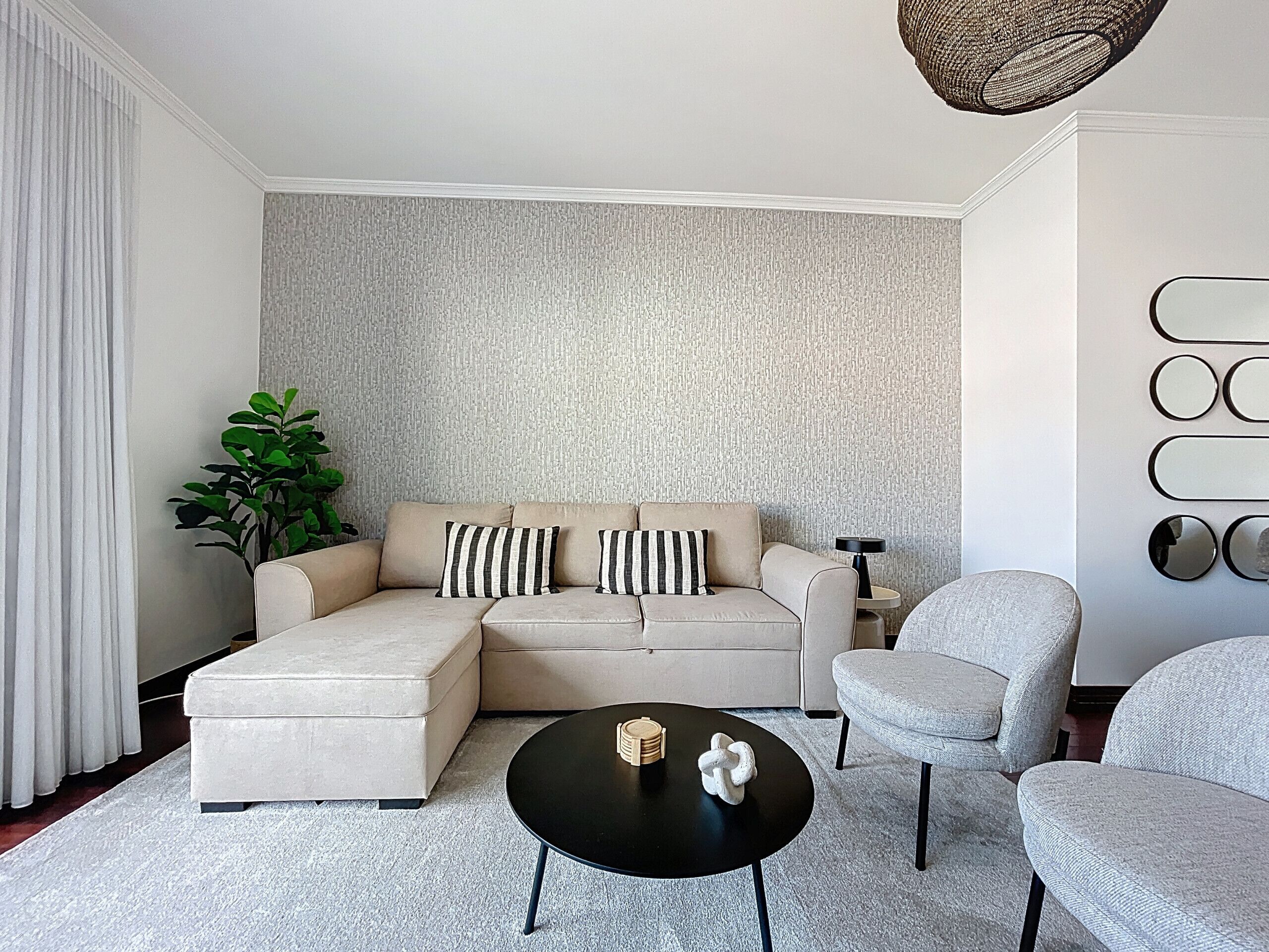 Un salon moderne avec un canapé d’angle beige, une table basse ronde noire et un fauteuil gris.