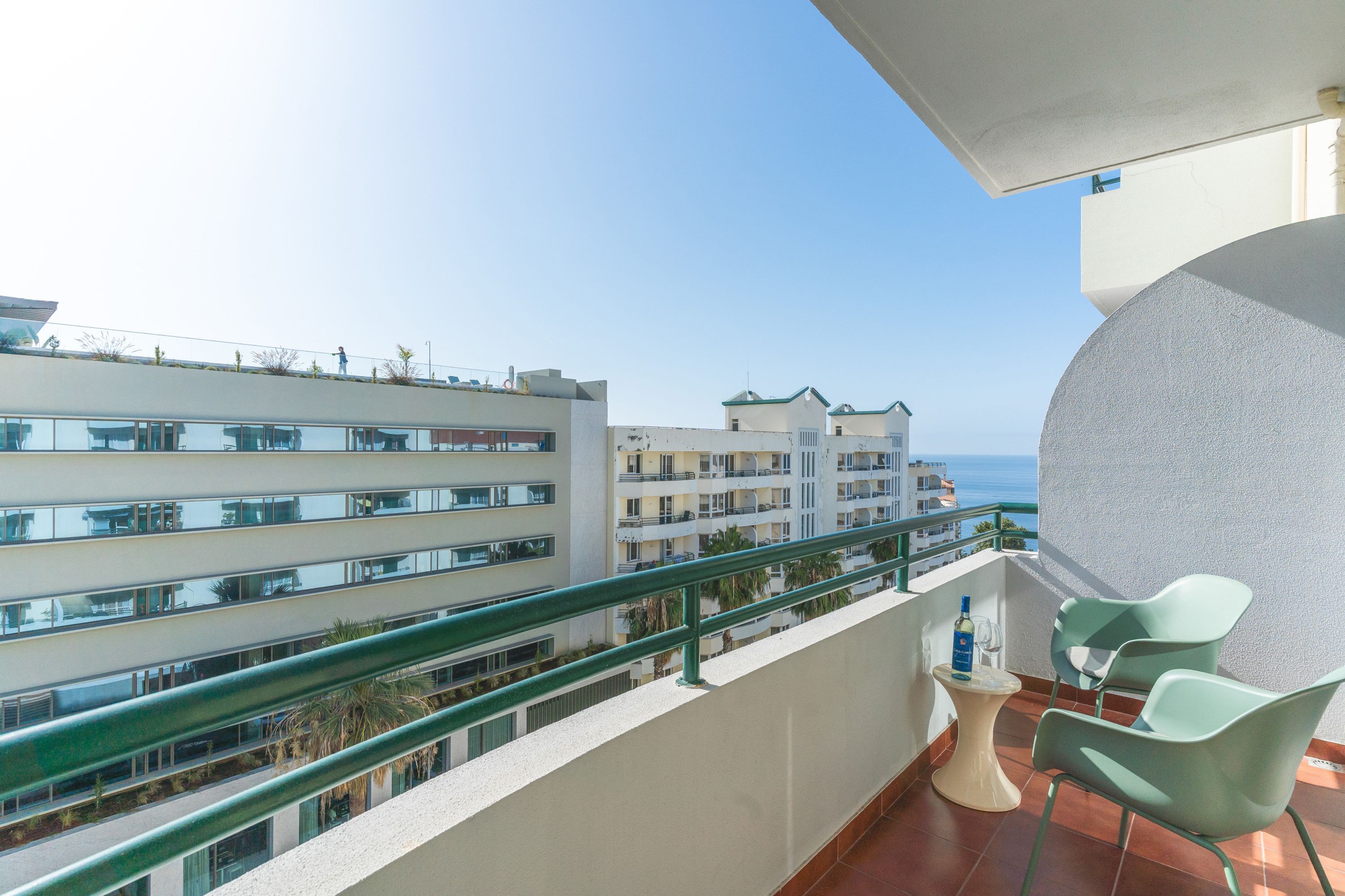 Un balcón con mesa y sillas, con vistas a una zona costera con edificios y cielo despejado.