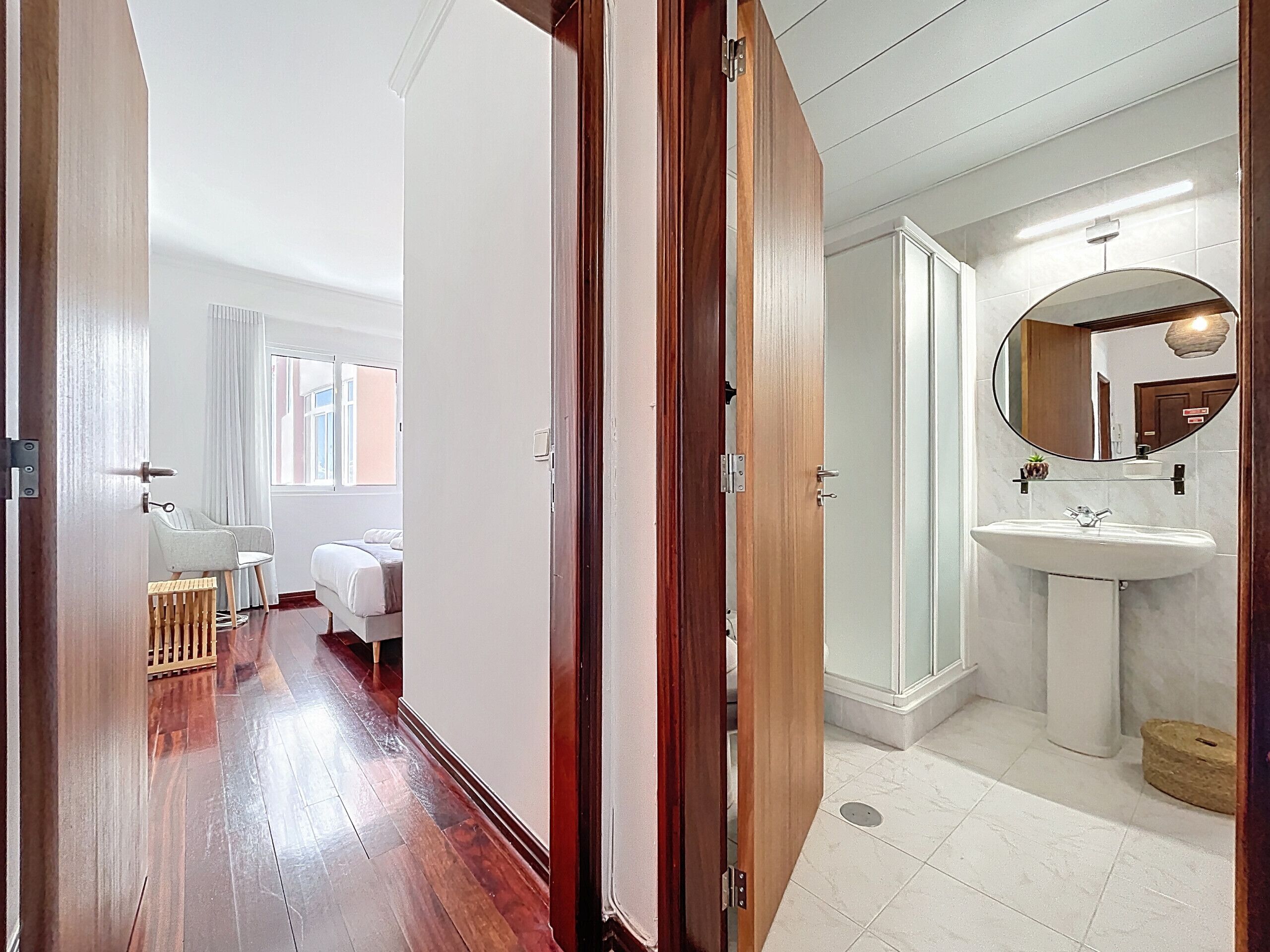 A hotel room with a wooden floor, a bed, a small table, and a window with curtains.