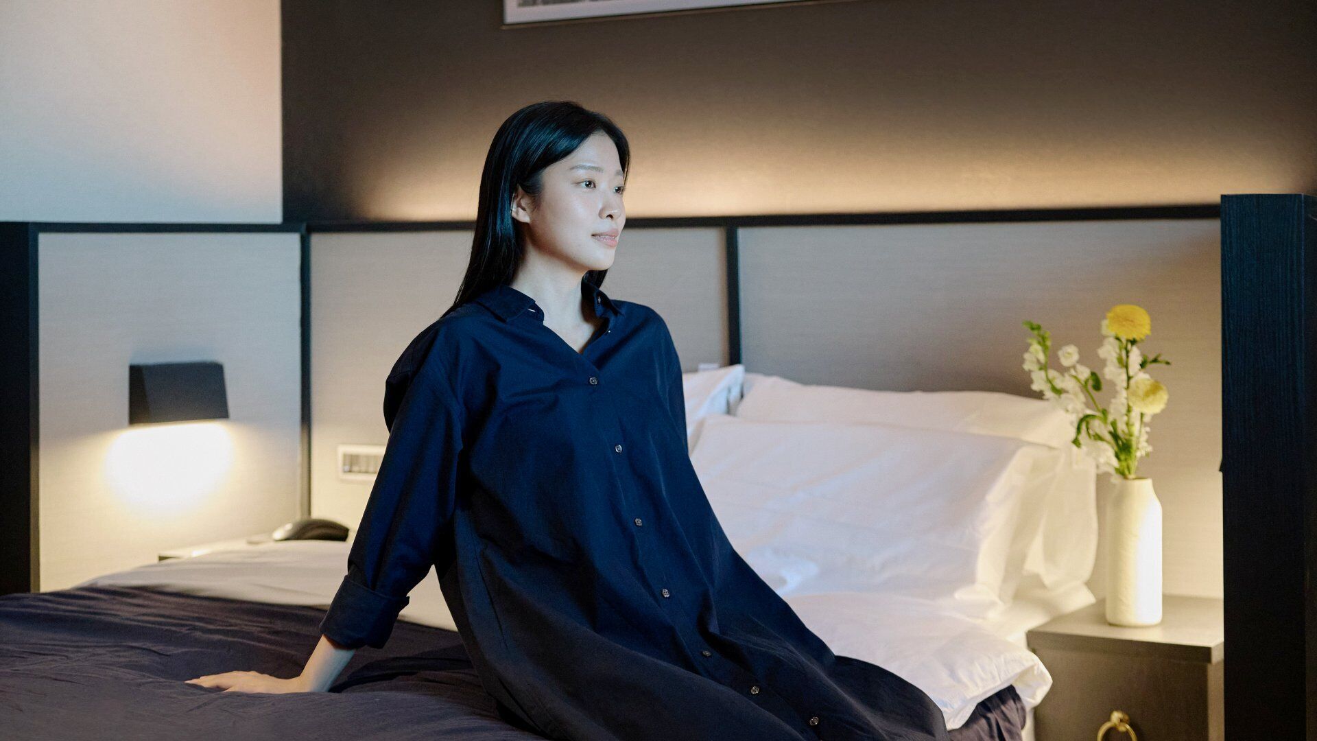 A hotel room with a bed, a nightstand with a lamp, and a vase with flowers.